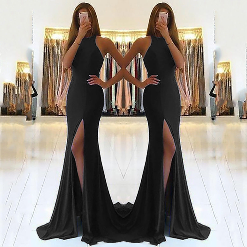 Woman wearing a black evening gown with a high slit in front of a mirror.