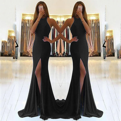 Woman wearing a black evening gown with a high slit in front of a mirror.